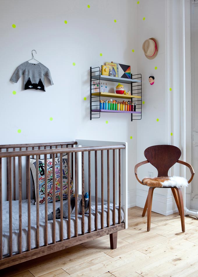 A stylish nursery room with a wooden crib and a chair besides it. Image by Cuckooland.