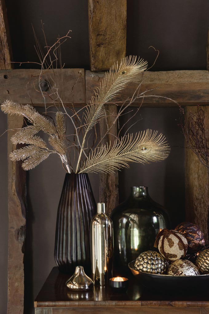 A beautifully styled vase on a sideboard along with other decor, filled with gold sticks and golden peacock feathers.