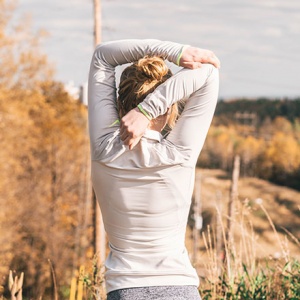 a woman's rear side while she's stretching her arm behind her head somewhere outdoors.