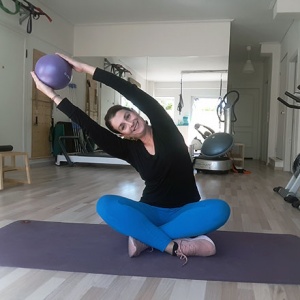 Ifiyenia holding a ball up while seated on a yoga mat just before her ball workout.