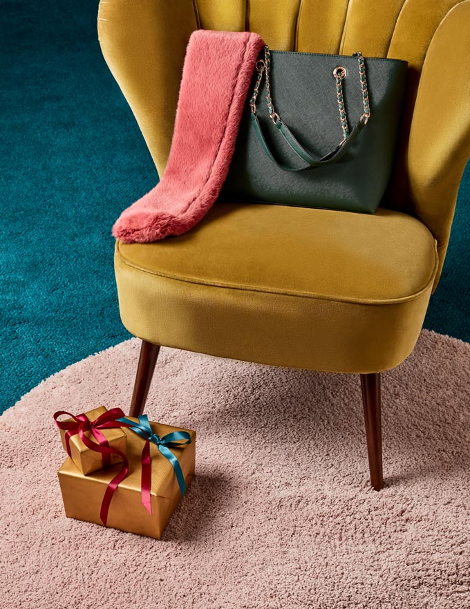 A mustard velvet armchair with a forest green bag atop and a coral scarf seem to fuse really well together colorwise. Image by Dorothy Perkins.