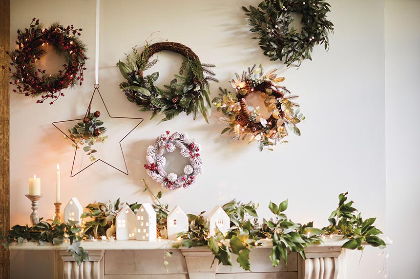 I love a white Christmas village with a garland as decor on a fireplace mantel, but the beautiful wreaths above it are stealing all the glory. Image by Marks & Spencer.