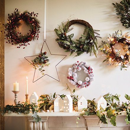 I love a white Christmas village with a garland as decor on a fireplace mantel, but the beautiful wreaths above it are stealing all the glory. Image by Marks & Spencer.