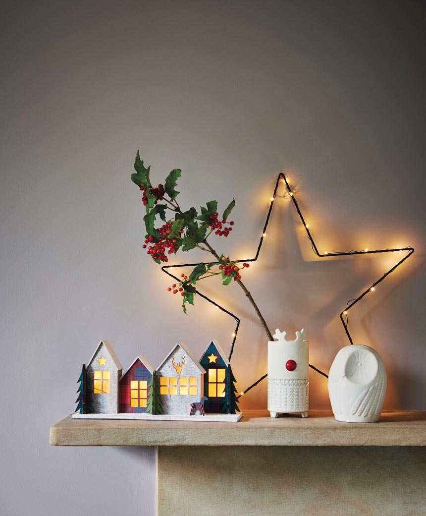 A little wire star as decor upon a mantle along with a Christmas village and a holly berry branch. Image by Next.