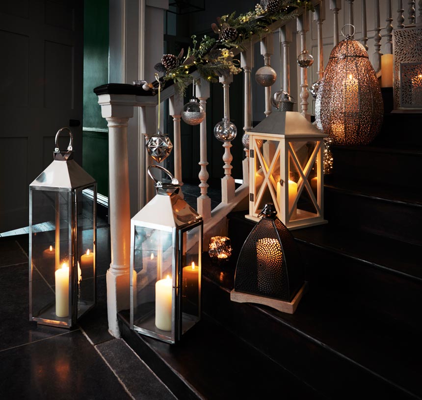 A clutter of lanterns along a home staircase with all the candles lit. Image by Next.
