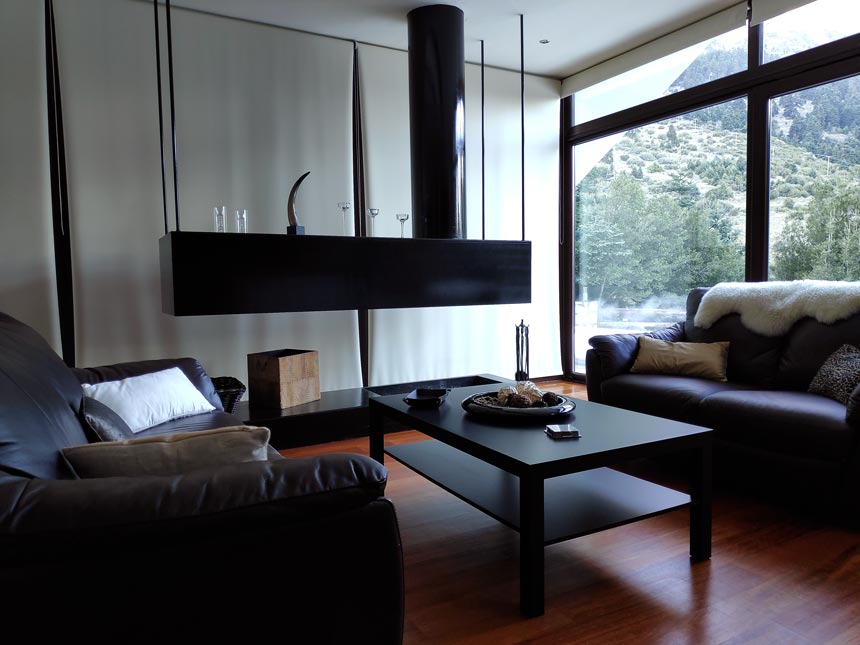 View of the minimal living room with its open fireplace, outdoor views to the forest and leather sofas.