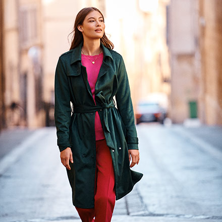 That's a fantastic looking outfit - a forest green sage trench coat over dark pink sweater and red pants. She looks stunning in a simple way. Image by Next.