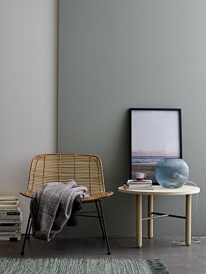 A minimal Scandi inspired vignette with a Dom by Bloomingville rattan chair next to a round side table decorated with books, a lamp and an art frame. Image by Lagoon.