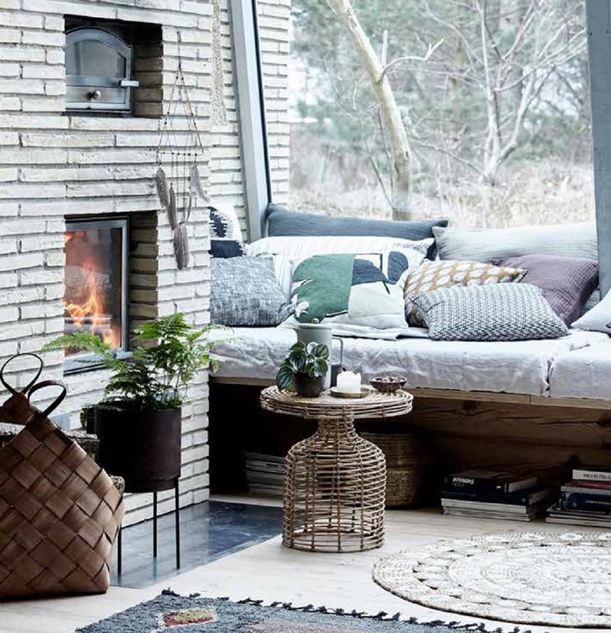 A living room with a fireplace and a large window on the side looks so charming with a real hygge feeling to it. The round rattan side table by House Doctor is the detail that adds a vintage charm to it all. Image by Lagoon.