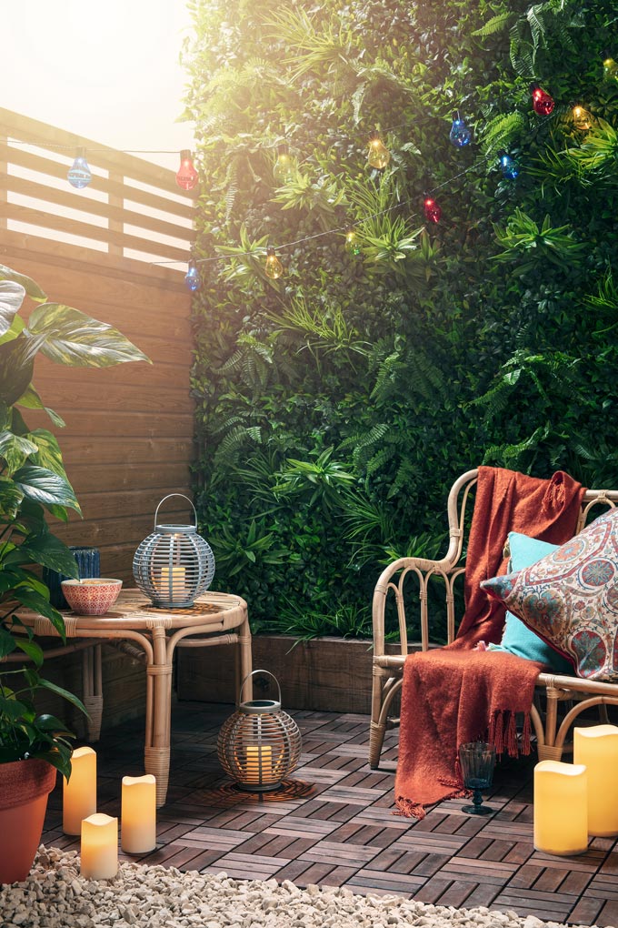 Candles and rattan lanterns add such warmth even in an outdoor space. An outdoor vignette with a rattan sofa and side table and blanket thick green foliage in the background looks a lot like a place I want to have for myself. Image by ©Lights4fun.