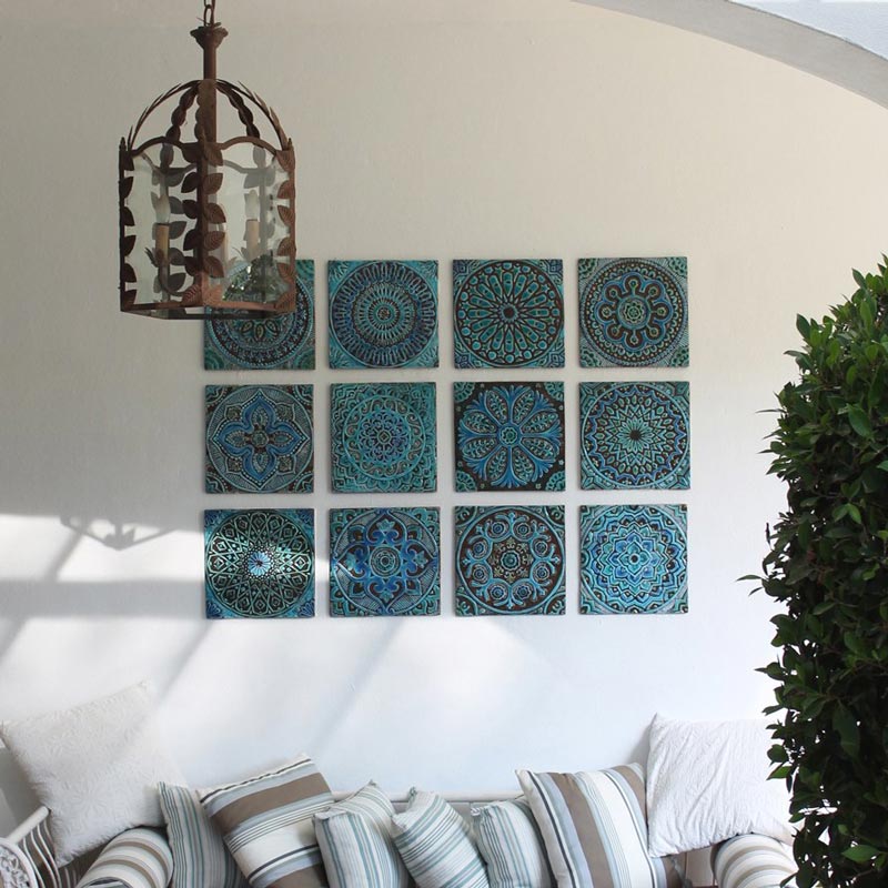 A covered roof outdoor space with a boho vibe and a sofa against a wall that features three rows of decorative handmade turquoise tiles. Image by G. Vega.