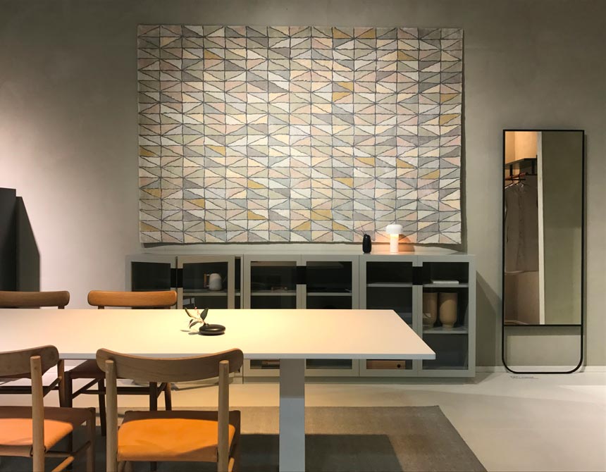 Partial view of a dining space with a wall tapestry at the stand of Asplund at imm Cologne 2019. 