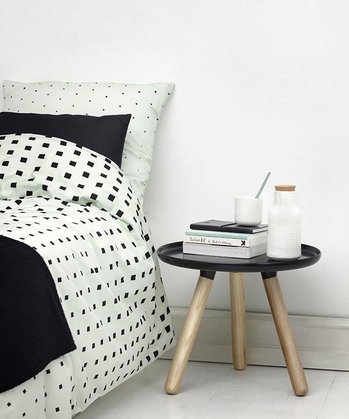 Side view of a contemporary bed with minty colored bedding with a black cube pattern on them. Image by Nest.