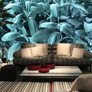 View of a stunning living space with a magnified blue green leafy accent wall as a background to a pattern print sofa. This image is from the stand of Poliform at the imm Cologne 2019 fair.