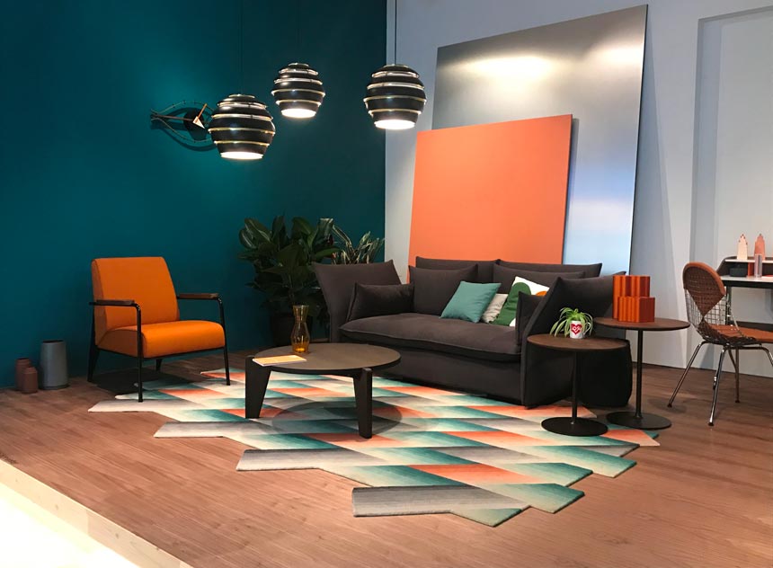 A contemporary living space with a dark sofa and an orange like armchair besides it. One of walls is in a deep teal color making an excellent backdrop for the armchair. This is part of the stand from Vitra at the imm Cologne 2019 fair.