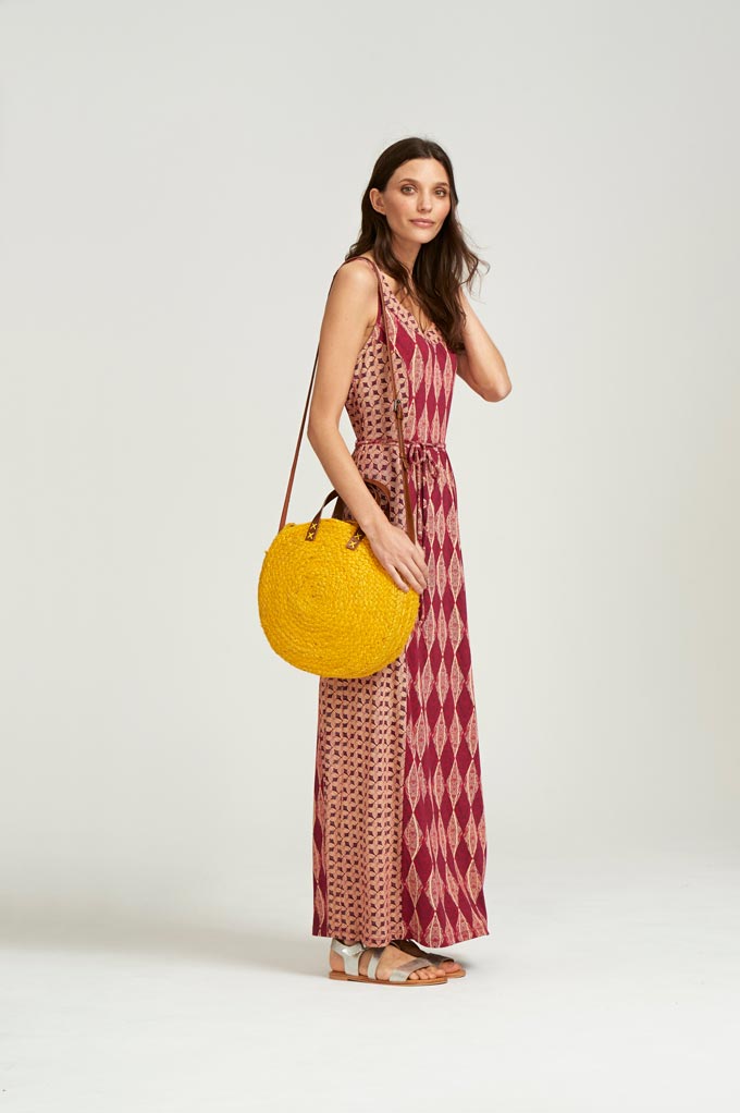 A maxi print sleeveless dress paired with a mimosa yellow, round straw bag. Image by Whitestuff.