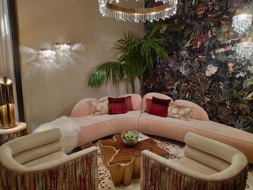 A luxurious living room with a blush pink curved sofa, an accent Mooi wallpapered wall and a coffee table that resembles the bark of a tree trunk by Brabbu Design Forces at iSaloni 2019 in Milan.