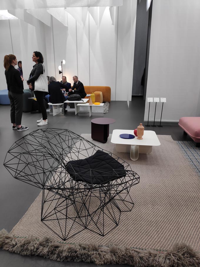 A black truss frame armchair on top of a neutral area rug with a coffee table in the background from the booth of LaCividina at iSaloni in Milan.