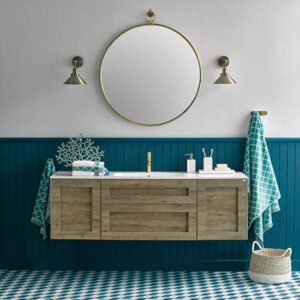A contemporary bathroom where teal reigns in the wainscotting and flooring. A brassy round mirror is paired nicely with two brassy sconces on each side of it. I like the wall mounted wooden tone vanity furniture that makes everything feel more airy. Image by El Corte Inglés Decoración.