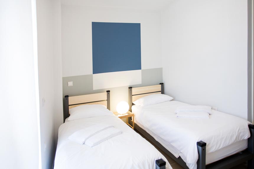 A twin bedroom designed by Velvet Karatzas for a renovation project of a hostel that has color blocking on an accent wall.