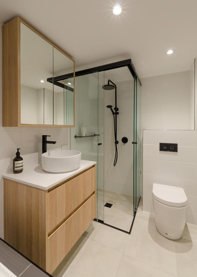 A contemporary bathroom with a wooden vanity furniture and a mirrored storage cabinet over the wash basin. What grabs my attention though are the black fittings, especially in the shower. Image by Meir Australia Pty Ltd.