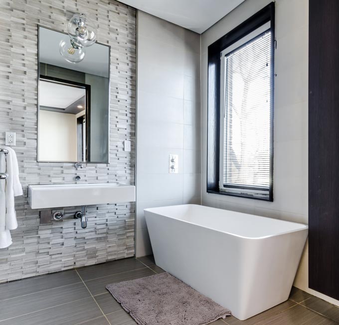 A contemporary bathroom with a textured accent wall behind the wall mounted washbasin and large bathroom mirror.