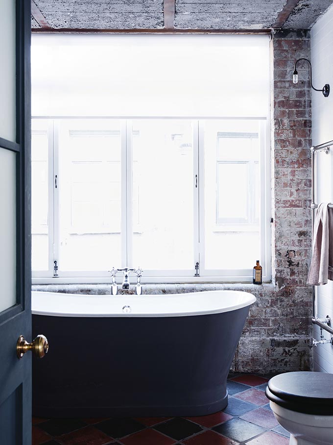 A free standing black tub by a large window with exposed brick walls is as industrial as I'll ever get. I love the simple design of the wall light. Image by Fritz Fryer.