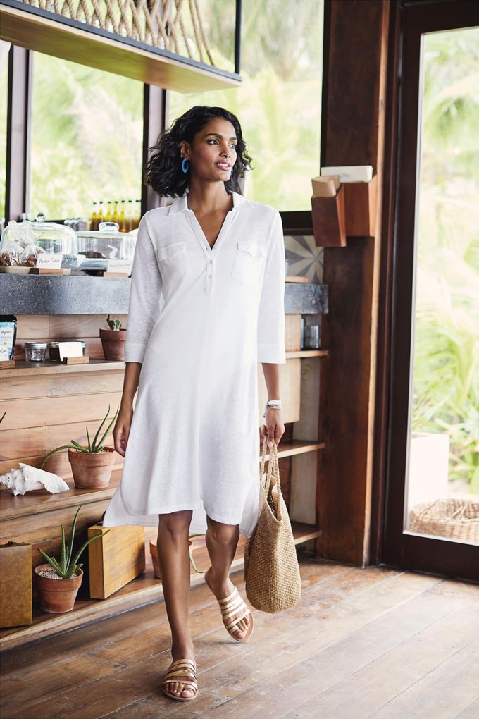 A white knee high dress with a very casual vibe paired with a large straw tote bag. Image by Pure Collection.