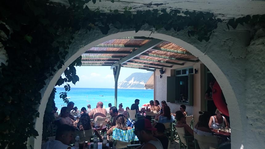 Sea view from a taverna's back patio with a coffee shop in front.