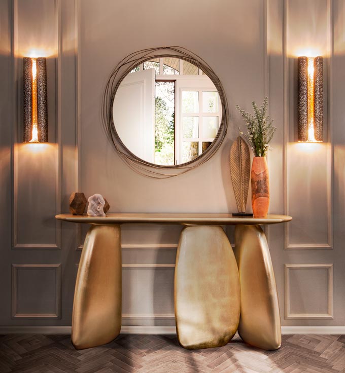 A beautiful round mirror over a stunning console table that resembles large golden boulders. The two wall sconces complete this vignette. Image by Brabbu Design Forces.