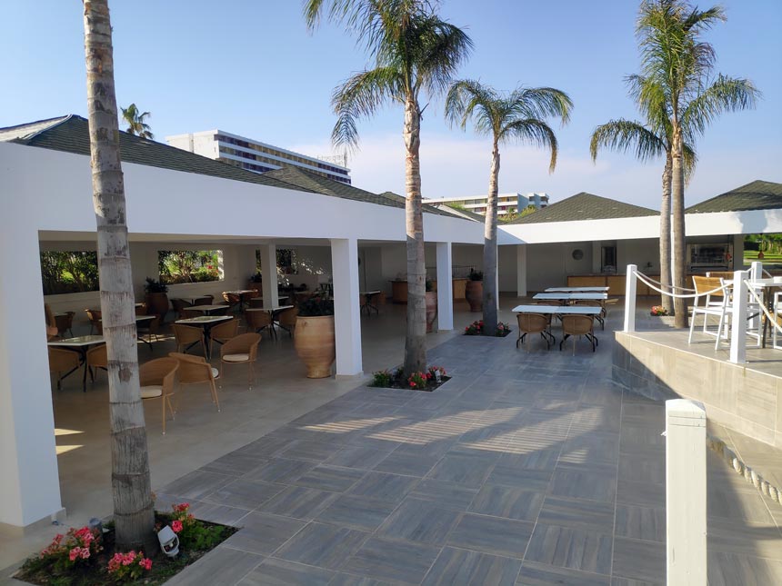 Partial view of the outdoor dining space under a pergola of the Greek restaurant at Grecotel Lux Me Rhodos.