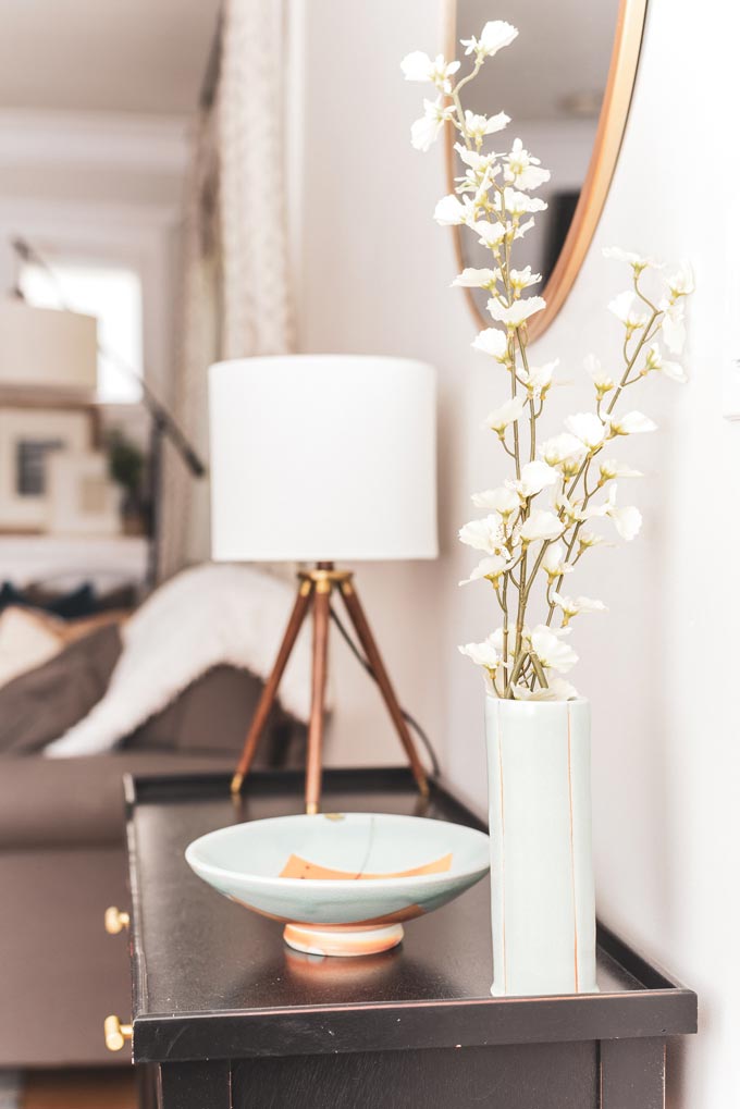 Side view of a vignette with white decor over a wooden sideboard against an off white wall.