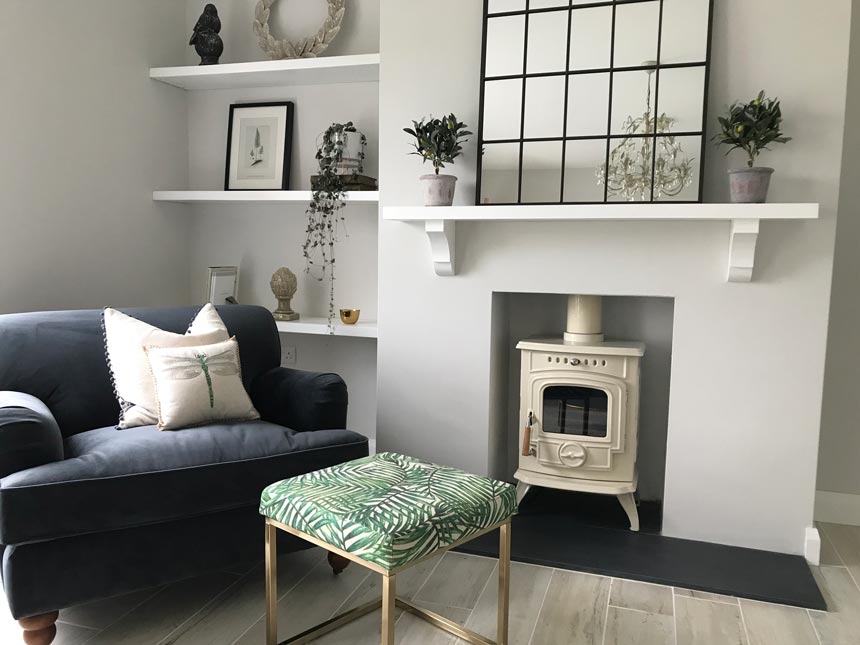 A paneled mirror over a fireplace in a contemporary living room with a blue sofa and a tropical leaf print pouf. Image by Cult Furniture.