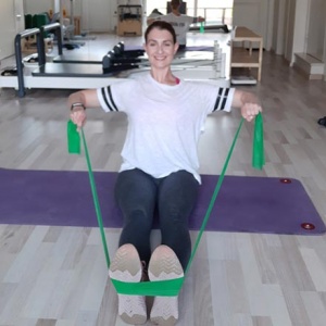 Ifiyenia doing a rowing exercise with a resistance band in a workout that targets the upper body.