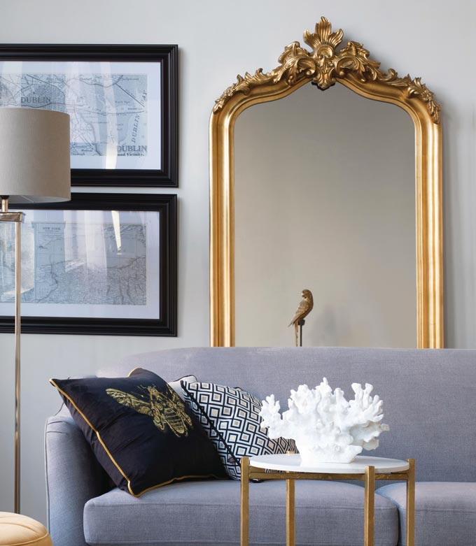 How to choose the perfect mirror: a large mirror standing behind a grey sofa next to two black frames. The setting is contemporary yet with lots of interesting juxtapositions. Image by Harvey Norman.