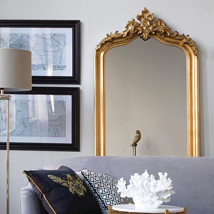A large mirror standing behind a grey sofa next to two black frames. The setting is contemporary yet with lots of interesting juxtapositions. Image by Harvey Norman.