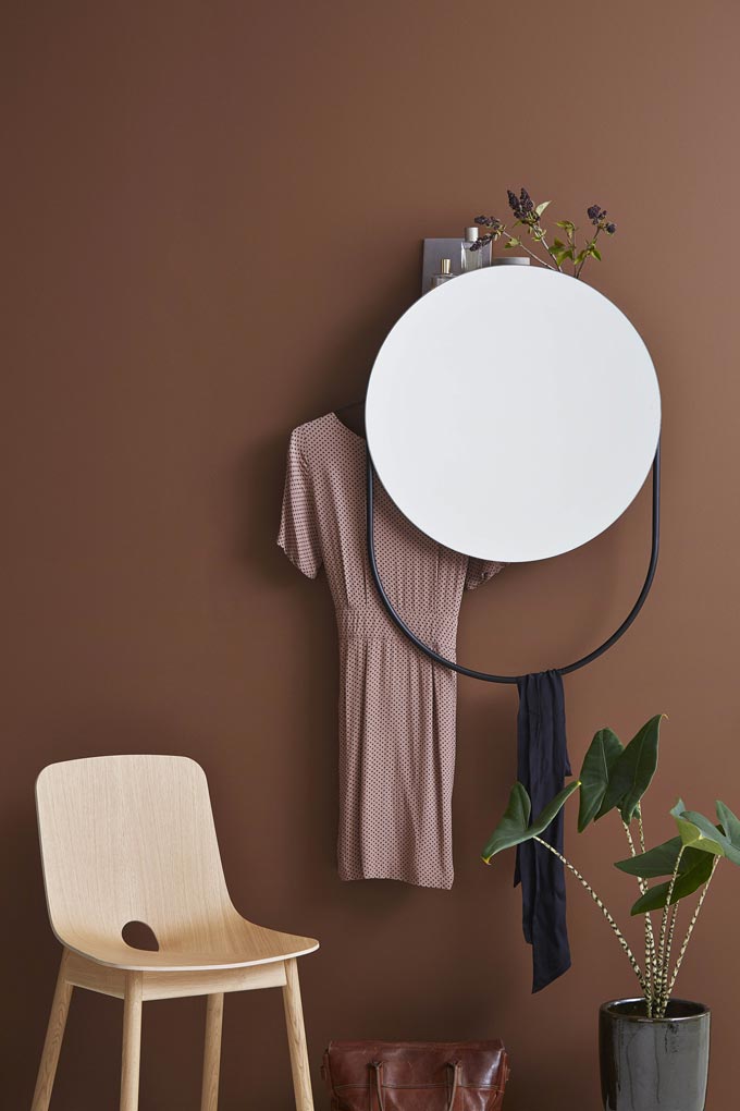 A round mirror that double serves as a hanger as well against a rusty hue wall. Image by Nest.