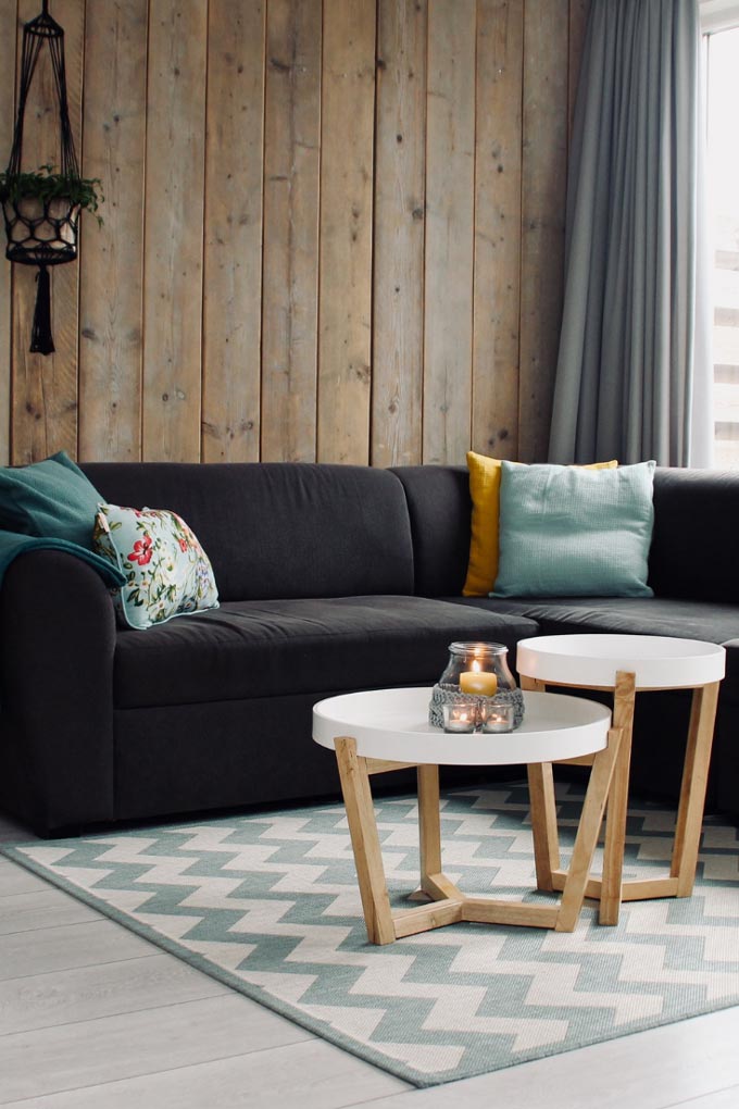 A black sofa in front of an wooden accent wall, sitting on top of an area rug with a chevron pattern.