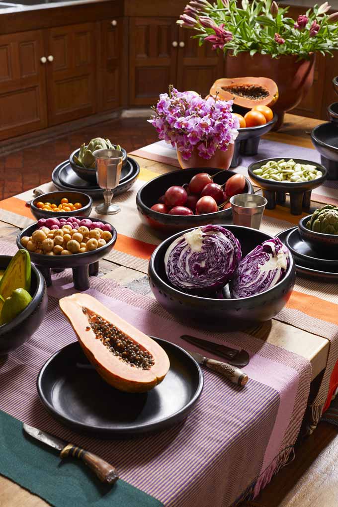 A table with barro black ceramic bowls and platters filled with veggies.