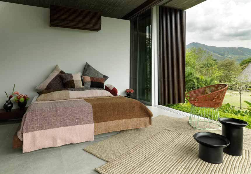 A bedroom with an incredible tropical forest view and an organic vibe to it because of all the textiles used as bedding from ames vibrant living.