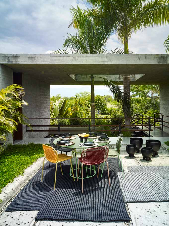 An outdoor dining set in front of a contemporary ground floor building with a hole on the concrete roof slab for the palm trees to go through.