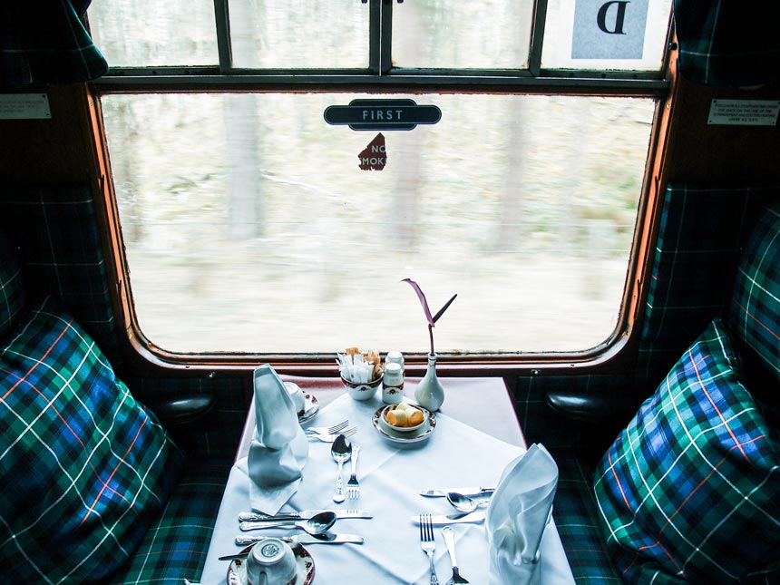 The inside of an old first class train car with plaid patterns on the seating benches and pillows.