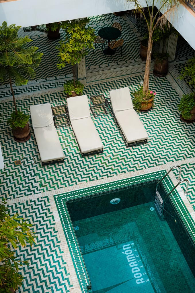 A swimming pool with three sunbeds on one end and a chevron pattern tiled flooring.