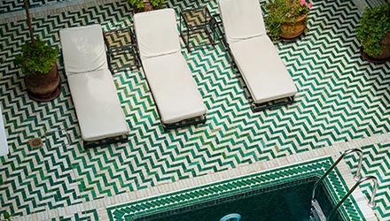A swimming pool with three sunbeds on one end and a chevron pattern tiled flooring.