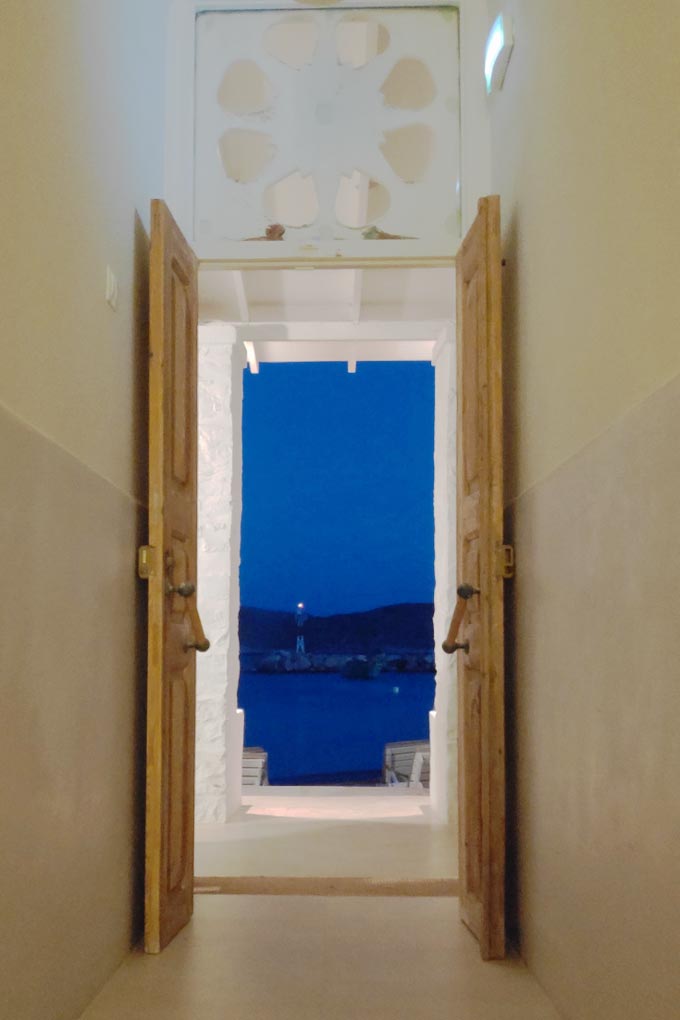 Cycladic minimal style: View from the corridor at the reception area and through the wide open main door, looking out to the beacon across the dock in the background.