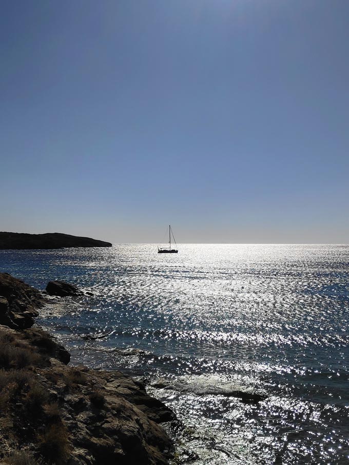 The silhouette of a sailing boat in a sea under midday's summer sun.