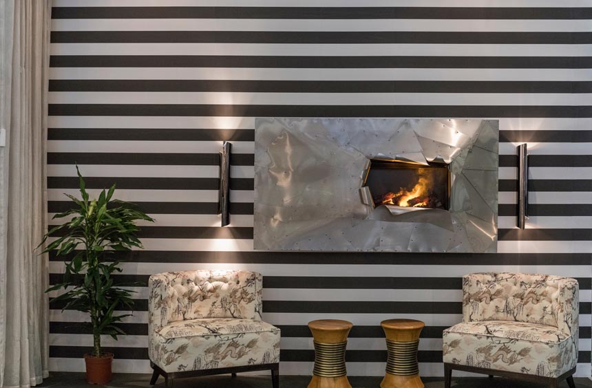 A horizontal black and white stripe wall treatment with a fireplace insert and two armchairs in a velvet print creating a striking composition. Image via