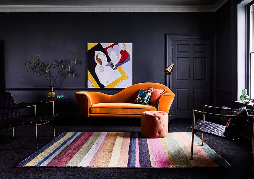 A inky grey room with a statement rusty hue sofa over a multicolored striped area rug. Image by Carpetright.
