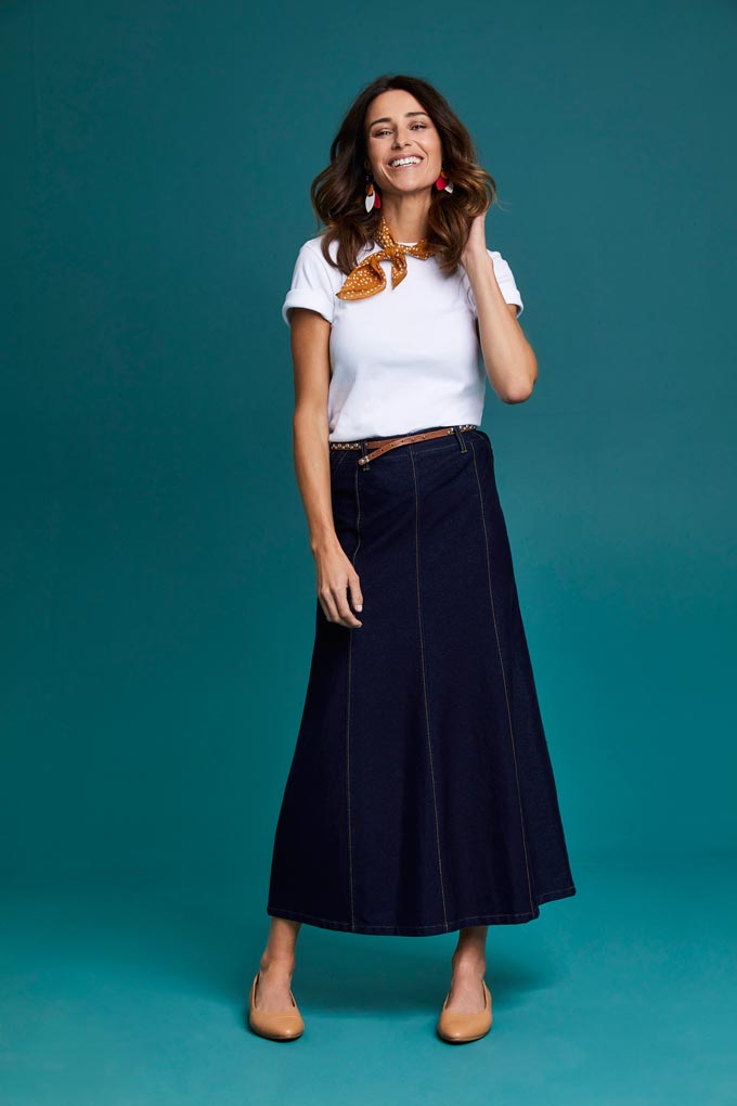A woman wearing a white tee over a maxi dark denim skirt along with some tan leather ballerina shoes. Image by Cotton Traders.