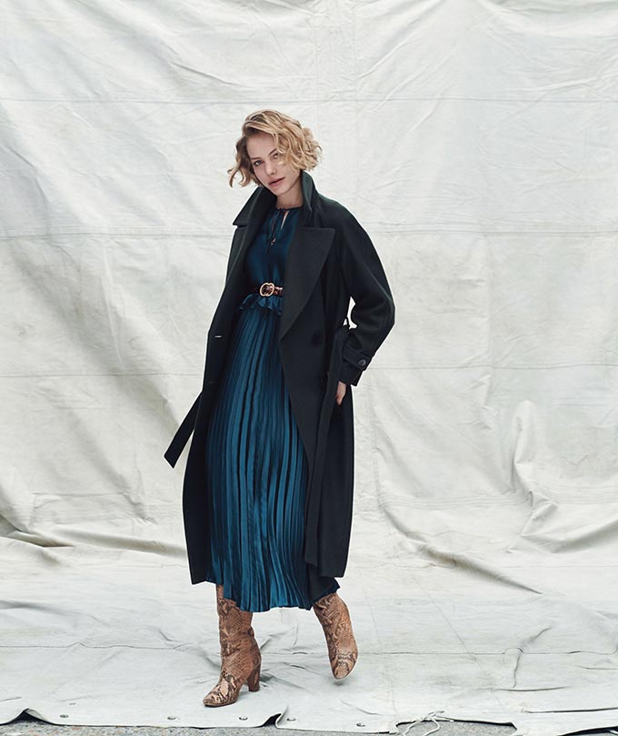 Fall fashion ideas: A dark blue teal top over a pleat skirt paired with beige suede boots and a dark coat. Image by Dorothy Perkins.